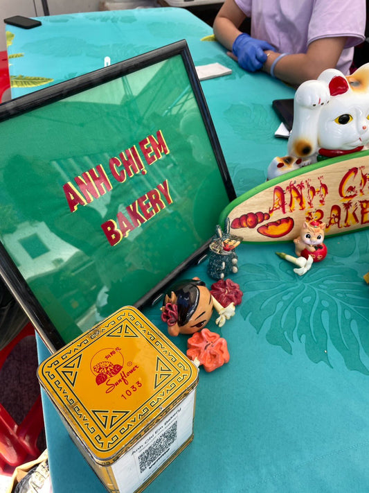 Anh Chi Em Bakery table with framed sign, lucky cat and decorations at a Honolulu market
