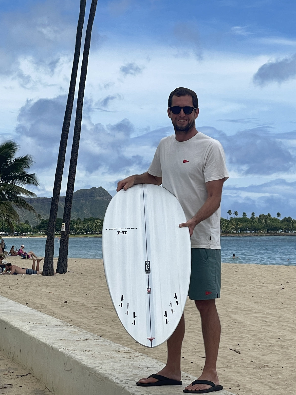Harley Ingleby holding the Harley Ingleby Mid 4 surfboard at Ala Moana Beach, Honolulu, showing the bottom and fin boxes