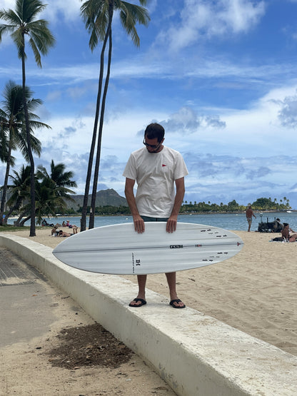 Harley Ingleby holding the white Harley Ingleby Mid 4 surfboard flat to show the deck at Ala Moana Beach, Honolulu
