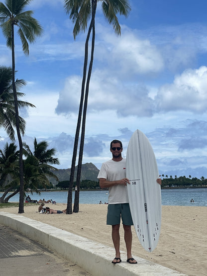 Harley Ingleby with the Harley Ingleby Mid 4 surfboard under palm trees at Ala Moana Beach, Honolulu