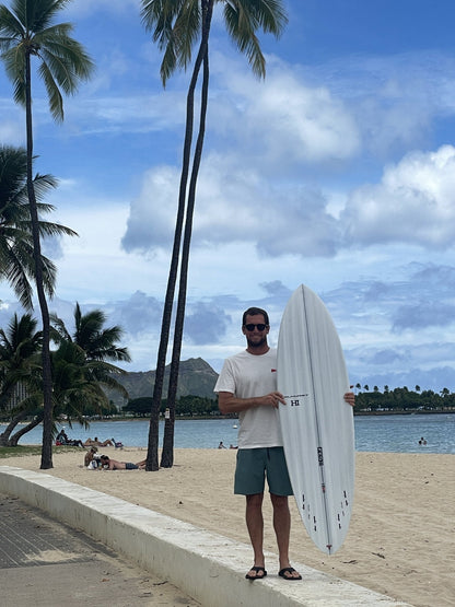 Harley Ingleby with the Harley Ingleby Mid 4 surfboard under palm trees at Ala Moana Beach, Honolulu