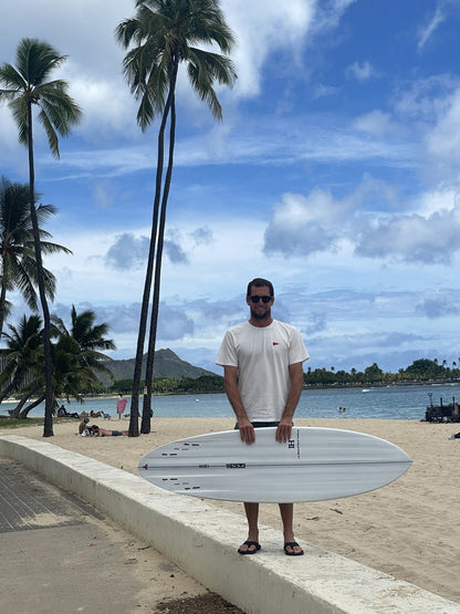 Harley Ingleby holding the Harley Ingleby Mid 4 surfboard horizontally at Ala Moana Beach, Honolulu